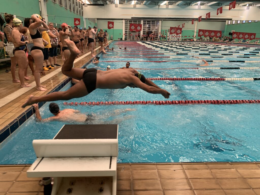 Ecoswim natação prova de revezamento. Em primeiro plano uma pessoa mergulha. 