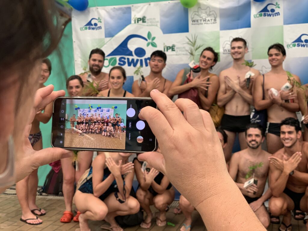 grupo de nadadores segurando mudas posam para foto feita pelo celular